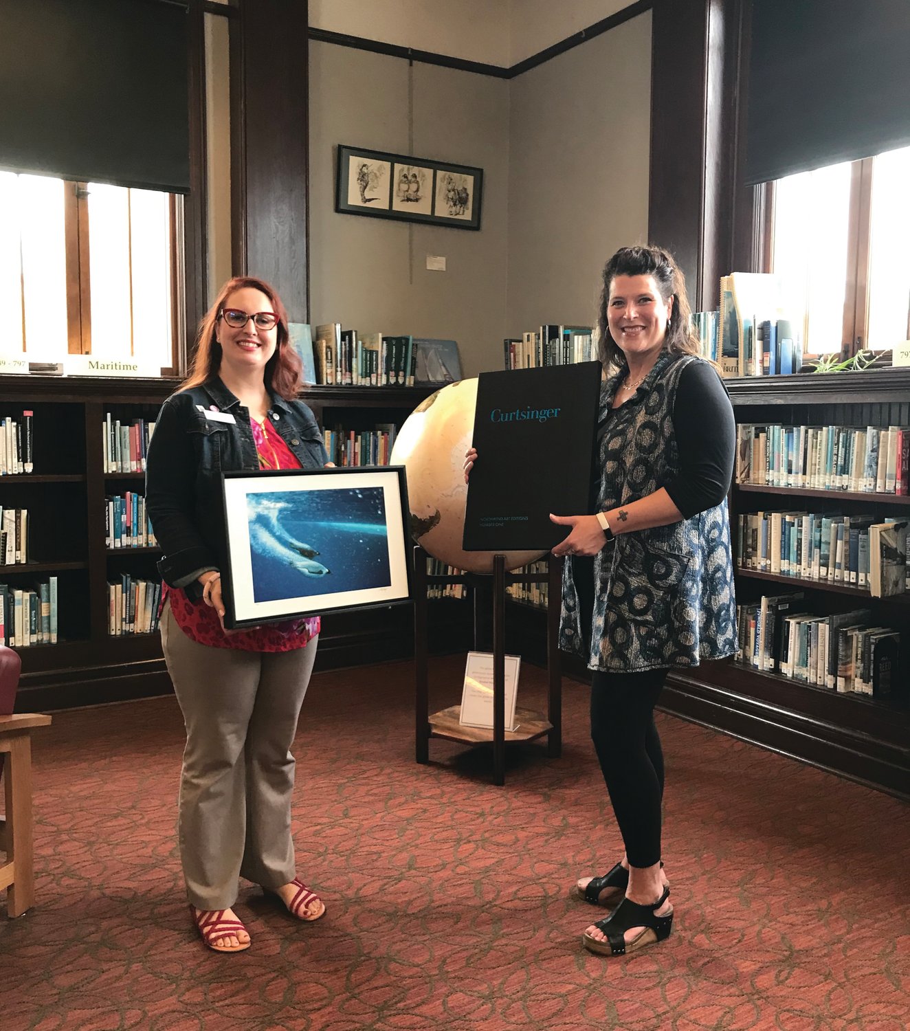Library Director Melody Sky Weaver poses with the recently donated Curtsinger Portfolio art as executive director Teresa Verraes presents the framed pieces to her at the Port Townsend Public Library.